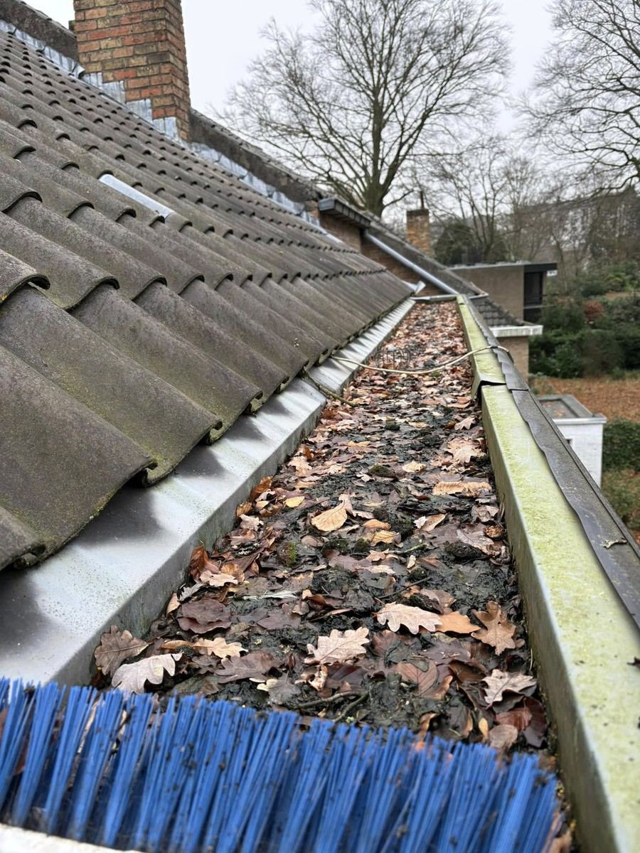 Dakgoot vol bladeren met een borstel van de reiniging