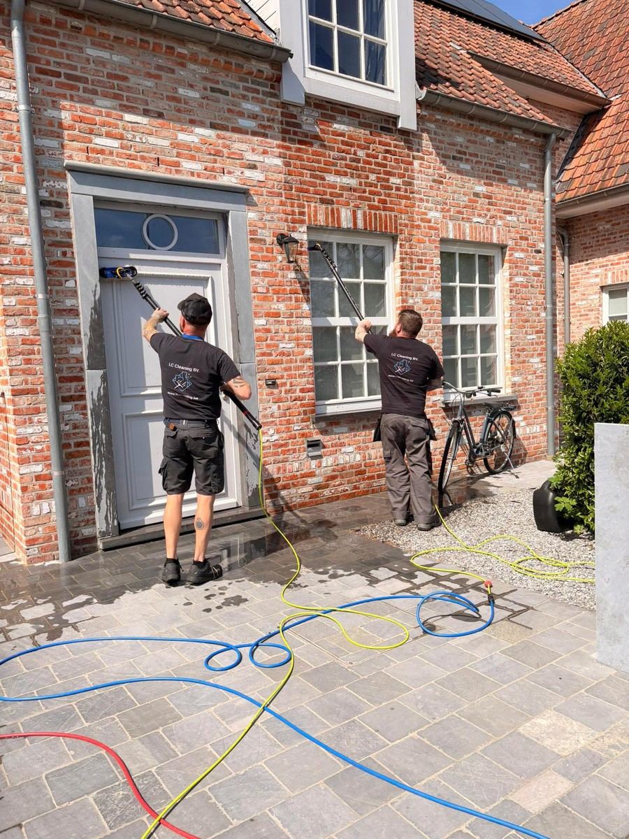 Twee medewerkers reinigen de gevel van een bakstenen woning